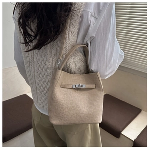 Detail of beige lychee textured bucket bag with silver twist lock and leather strap