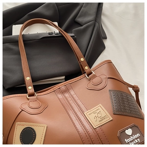 Close-up of brown PU leather tote bag with retro decorative patches and metal rivets