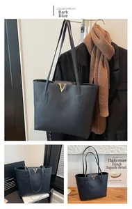 Detail of dark blue faux leather tote bag featuring gold V-logo and twin shoulder straps