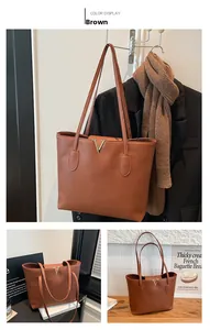 Detail of a brown lychee pattern leather tote bag featuring a golden V-shaped metal buckle