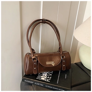 Détail du sac bowling en cuir marron foncé avec pendentif coeur sur des livres anciens