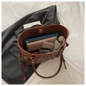 Detail view of the spacious interior of a brown tote bag holding an iPad, notebook, and phone
