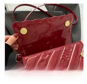 Detail of red patent leather shoulder bag featuring a magnetic clasp and embossed logo