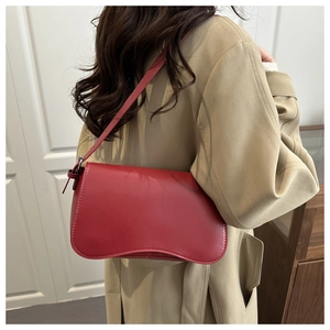 Borsa sottobraccio rossa minimalista indossata da una modella con un trench beige classico