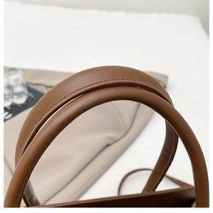 Dettaglio dei manici di una borsa marrone con cuciture rinforzate e texture a grana