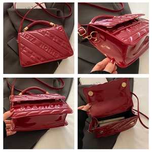 Detail view of red glossy patent leather handbag with embossed fashion lettering and gold handle