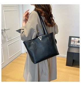 Detail of black lychee grain leather tote bag with silver V hardware on khaki trench coat