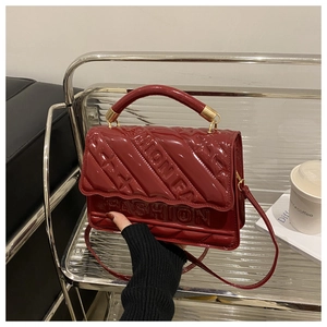 Detail of burgundy patent leather bag with diamond quilting and embossed fashion text
