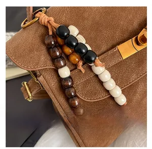Detail of beaded bag charm with wooden beads and gold keyring on brown leather bag