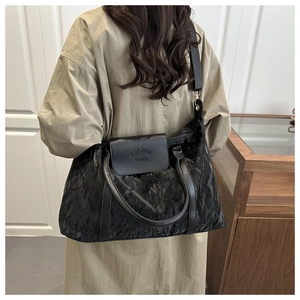 Detail of black tote bag with textured wrinkled fabric and branded leather flap