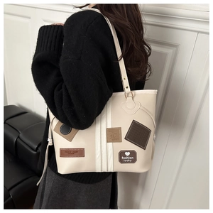 Detail view of large cream tote bag with fashion leather patches on model shoulder