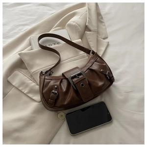 Retro dark brown pleated underarm bag with metal buckles and rivets on a beige blazer