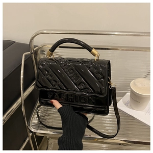 Close-up of black patent leather crossbody bag with FASHION embossed logo and gold hardware