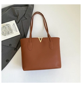 Flat lay of brown leather tote bag with V-shaped gold buckle and chic urban accessories