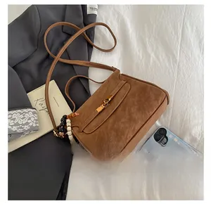 Detailed view of brown suede crossbody bag with vintage lock and beaded accessory on fabric