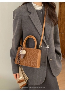 Detail of leopard print baguette bag with brown leather accents and plush charm