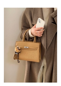 Close-up of leather handbag with metal turn-lock, plush charm, and woven texture detail