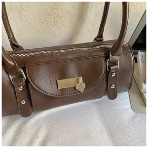 Close-up of a dark brown barrel bag with gold heart charm and top handle detail