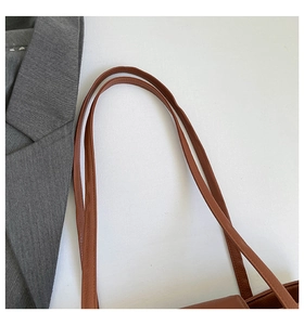 Detail of a brown leather shoulder bag strap with pebble texture and grey office blazer