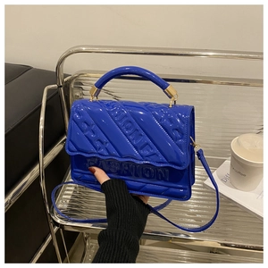 Close-up of royal blue glossy shoulder bag with embossed FASHION text and gold hardware