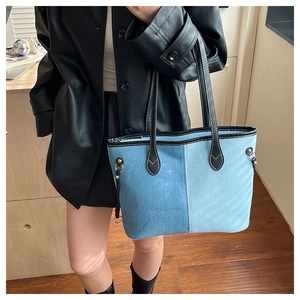 Detail of blue denim tote bag featuring vertical contrast stitching and metal ring accent