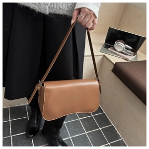 Dettaglio borsa a spalla in pelle marrone con base curva unica indossata da modella