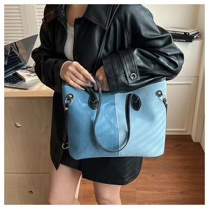Detail of light blue denim tote bag with black leather handles and golden metal rivets