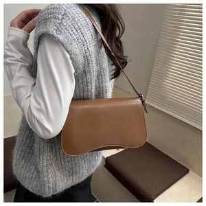 Dettaglio borsa a spalla in pelle marrone con fondo ondulato e design minimalista elegante