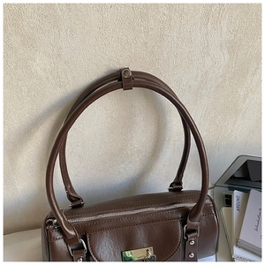 Close-up of deep brown leather Boston bag with silver heart pendant and metal hardware