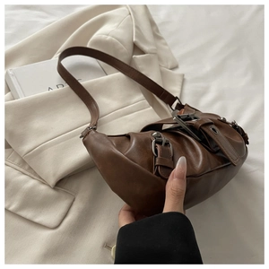Detail of dark brown vintage pleated leather tote with metallic buckles on white fabric