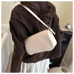 Dettaglio di una borsa sottospalla beige opaca con base curva e tracolla sottile