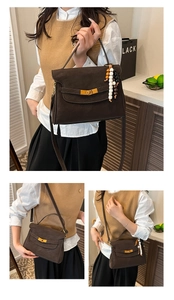 Detail of dark brown suede handbag featuring gold buckle and beaded tassel pendant
