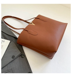 Detail of caramel brown tote bag with pebble leather texture and gold V-shaped metal hardware