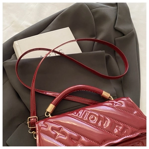 Detail of burgundy patent leather bag with embossed fashion texture on grey blazer