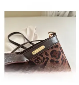 Detailed view of the leopard print fabric, dark brown leather trim, and golden logo plate