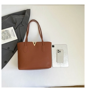 Flat lay of brown leather tote bag with V-shaped metal hardware and iPad for scale