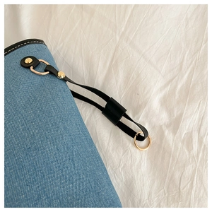 Detail of blue denim tote bag featuring black leather trim and gold metal hardware