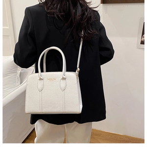Dettaglio borsa Boston bianca con trama a coccodrillo, logo dorato e doppi manici