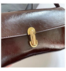 Detail of dark brown glossy leather baguette bag with metal clasp and pleated texture