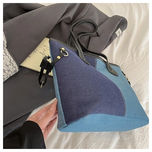 Detail of blue denim patchwork tote bag with asymmetric panels and leather handles