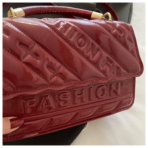 Macro shot of burgundy patent leather bag featuring embossed FASHION logo and gold hardware