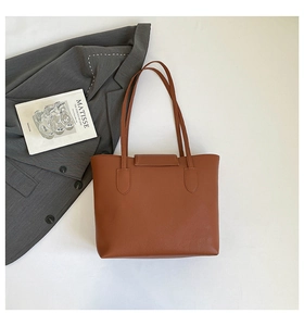 Detail of a brown leather tote bag with lychee texture next to a blazer and art book
