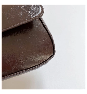 Detail shot of a dark brown baguette bag featuring glossy wrinkled leather and fine stitching