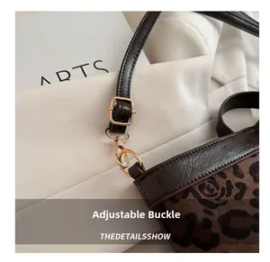 Detail shot of adjustable golden metal buckle and brown leather strap on leopard tote
