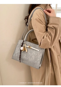 Détail d'un mini sac seau gris argenté avec poignées métalliques et pendentif de baseball