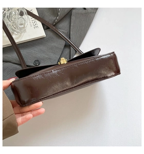 Detail view of the chocolate brown glossy leather baguette bag with golden metal hardware