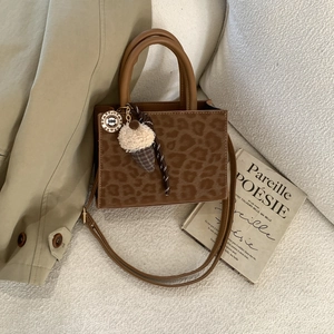 Leopard print crossbody bag with plush charm on a cozy white textured sofa background