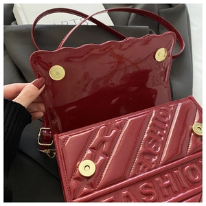 Detail of burgundy patent leather bag with embossed fashion text and golden magnetic clasp
