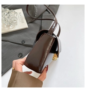 Close-up of glossy brown baguette bag with golden rotating metal lock and fine strap