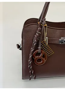 Detail of dark brown pebble leather handbag featuring a pretzel and abacus bag charm